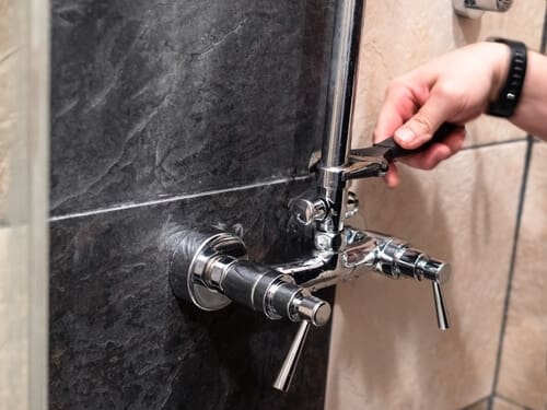 plumber installs shower pipe to faucet valve in shower room at home